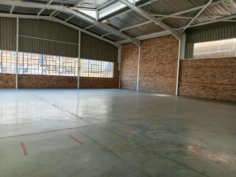 Spacious industrial warehouse unit featuring exposed brick walls, high steel-truss ceilings, polished concrete flooring, and large steel-framed windows providing ample natural light.