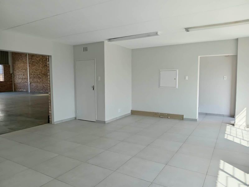 A clean, empty office space featuring neutral tiled flooring, white walls, and fluorescent lighting, providing a versatile area for industrial or commercial use.