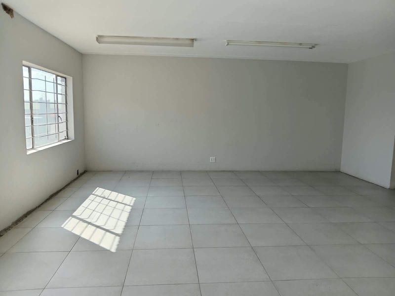 A vacant, open-plan office space featuring neutral tiled flooring, fluorescent lighting, and a window with security bars, ready for custom fit-out.