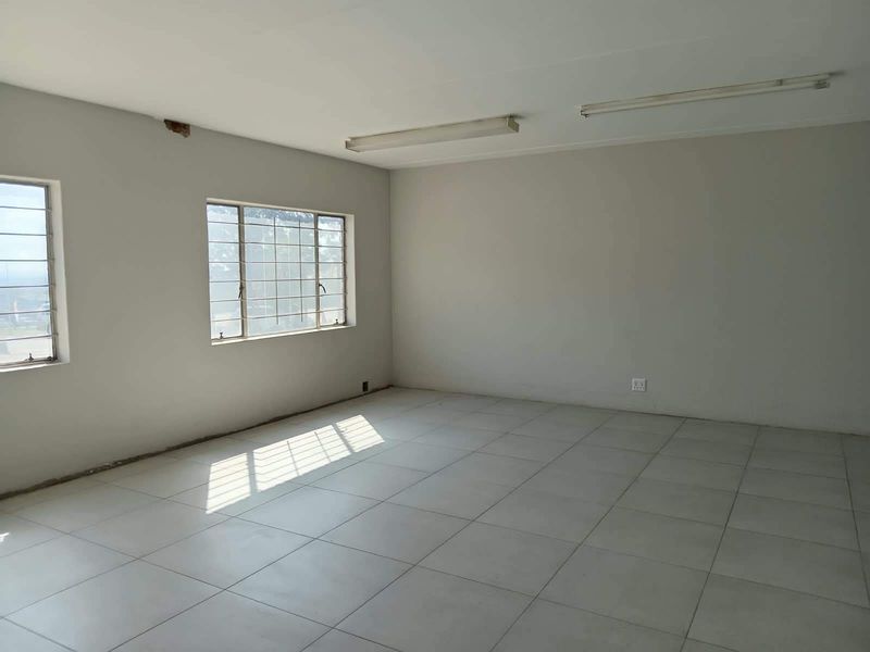 An empty, open-plan office space featuring tiled flooring, fluorescent lighting, and steel-framed windows, ready for customization.