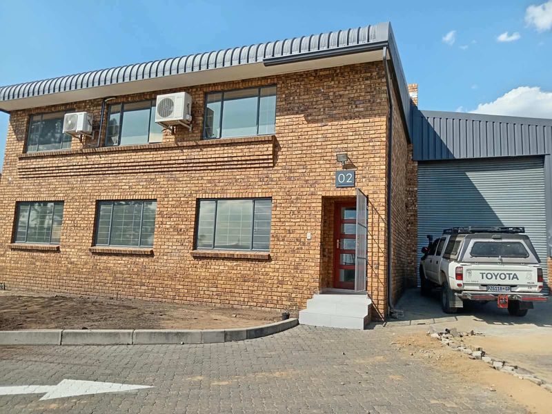 Front elevation of a two-story industrial building featuring face brick construction, aluminium windows, external air conditioning units, and a roller shutter door.
