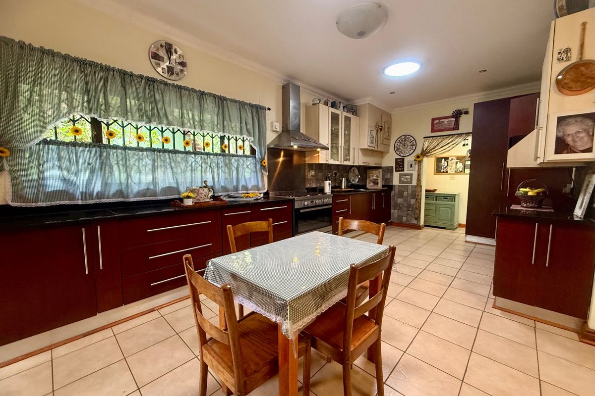 Spacious kitchen featuring dark wood cabinetry, granite countertops, stainless steel extractor fan, and tiled flooring, offering a functional layout for cooking and dining.