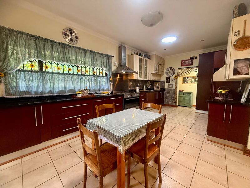 Spacious kitchen featuring dark wood cabinetry, granite countertops, stainless steel extractor fan, and tiled flooring, offering a functional layout for cooking and dining.