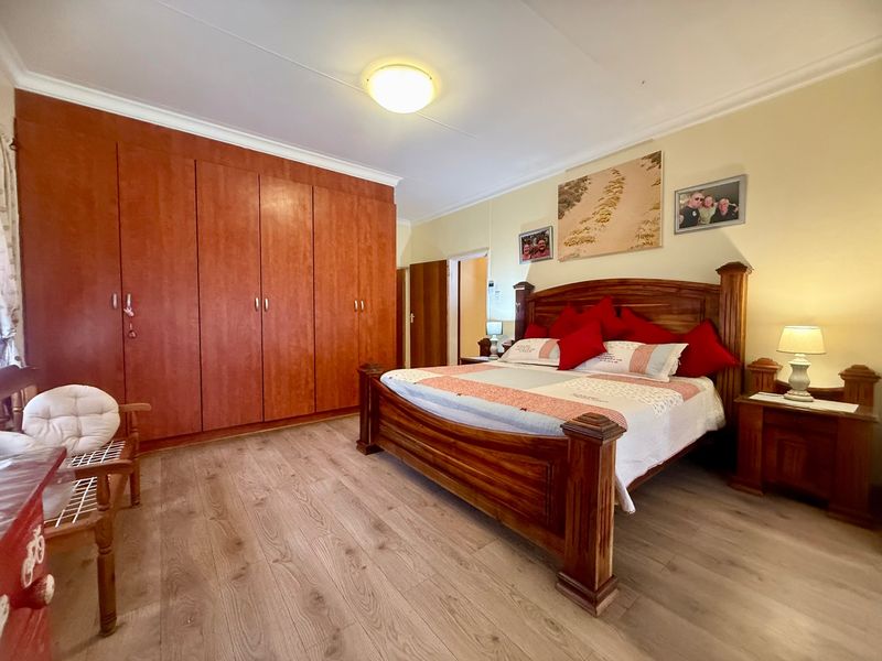 A well-maintained bedroom featuring warm-toned laminate flooring and extensive built-in wooden cupboards providing ample storage space.