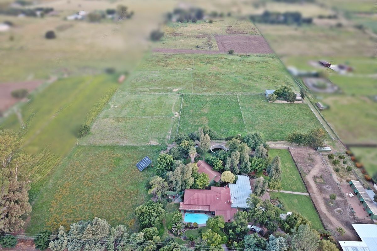 Aerial view of a farm property featuring a main residence with a swimming pool, solar panels, and extensive fenced paddocks.