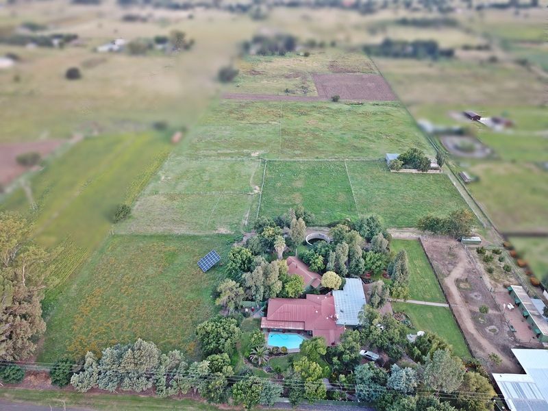 Aerial view of a farm property featuring a main residence with a swimming pool, solar panels, and extensive fenced paddocks.