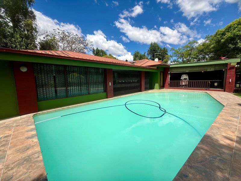 Outdoor pool area featuring a swimming pool with tiled surround, adjacent to a covered patio and the main building structure.