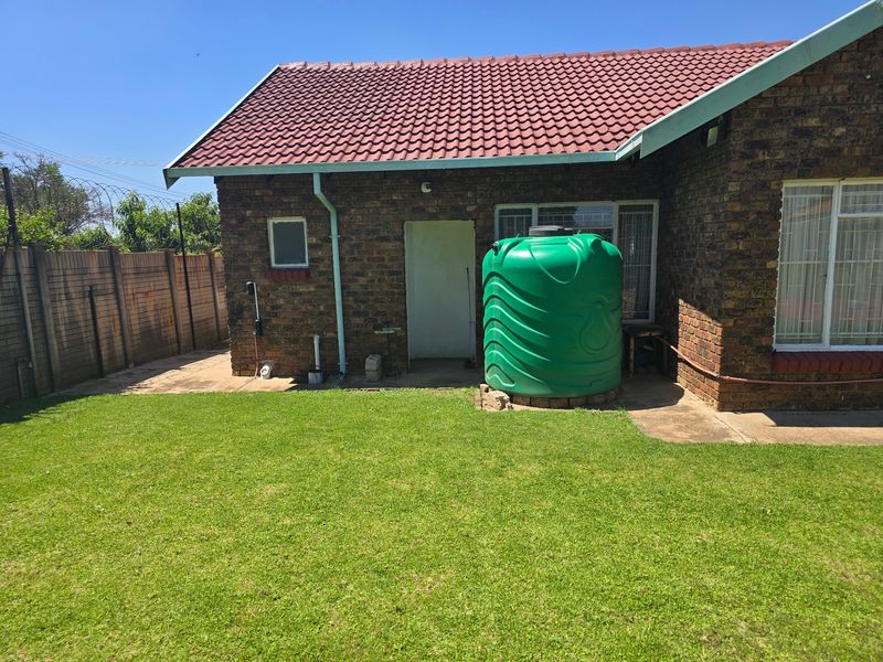 Rear exterior view of a face brick house featuring a tiled roof, a water storage tank, and a private garden with a paved patio area.