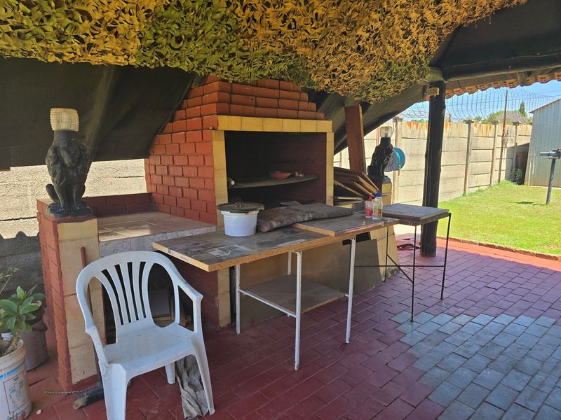 Outdoor patio area featuring a built-in brick braai, paved flooring, and a covered structure, providing a functional space for outdoor cooking and entertainment.