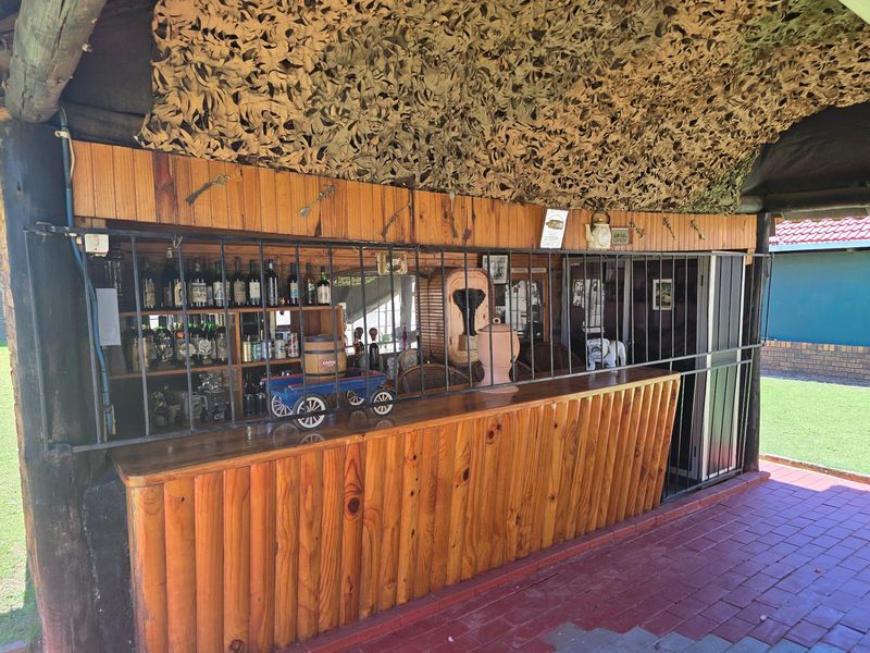 Outdoor entertainment area featuring a rustic built-in timber bar with security gate and brick paved flooring, covered by camouflage netting.