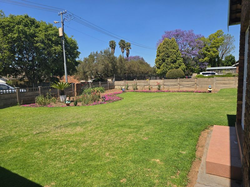 A well-maintained residential garden featuring a spacious lawn, landscaped flower beds, and a secure precast concrete boundary wall.