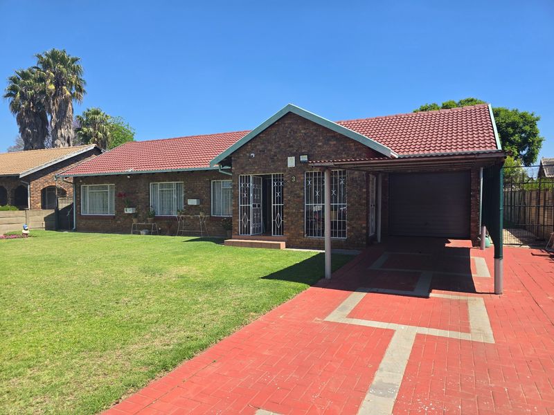 A well-maintained face brick house featuring a tiled roof, a paved driveway leading to a carport, and secure entrance gates.