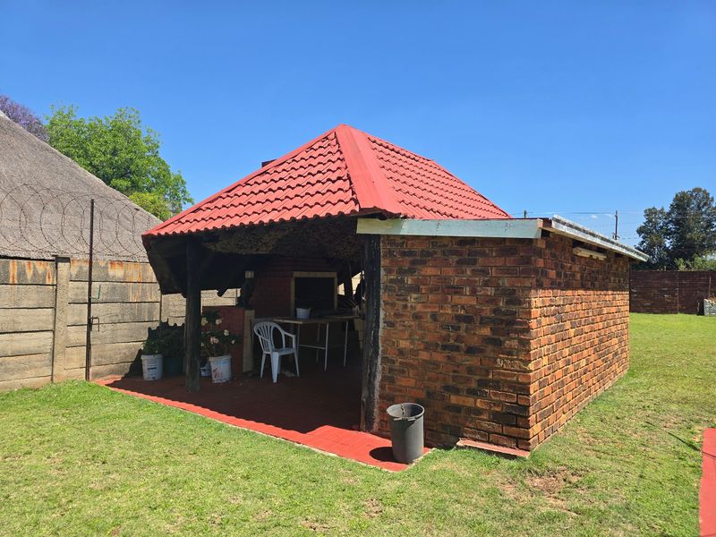 Outdoor covered patio area featuring a built-in braai, exposed brick construction, and tiled flooring, situated in a garden setting.