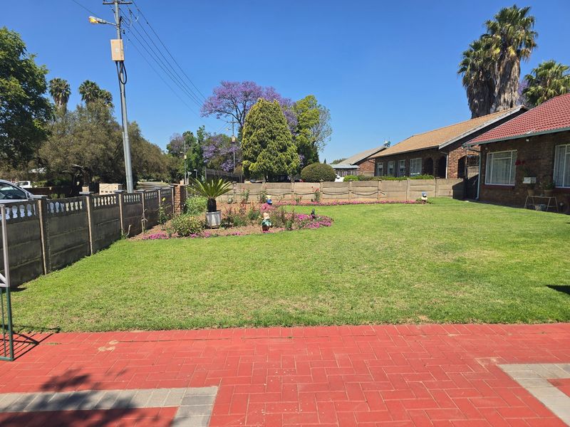 A well-maintained rear garden featuring a spacious lawn, landscaped flower beds, and a red paved patio area enclosed by precast concrete boundary walls.