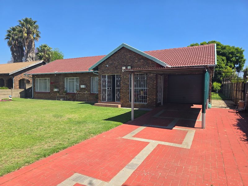 Front view of a face-brick house featuring a tiled roof, paved driveway, attached carport, and secure entrance with burglar bars.