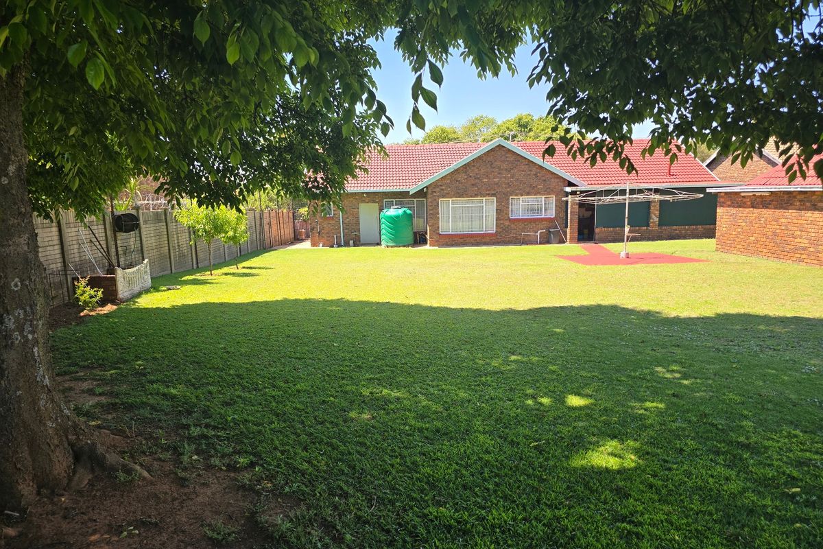 A spacious rear garden featuring a well-maintained lawn, brick exterior house facade, tiled roof, and a water storage tank.