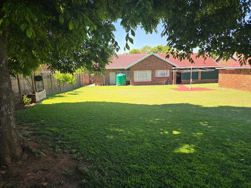 A spacious rear garden featuring a well-maintained lawn, brick exterior house facade, tiled roof, and a water storage tank.