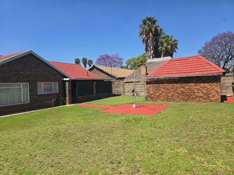 Spacious rear garden featuring a well-maintained lawn, face brick exterior walls, and a paved walkway connecting the main house to the outbuilding.