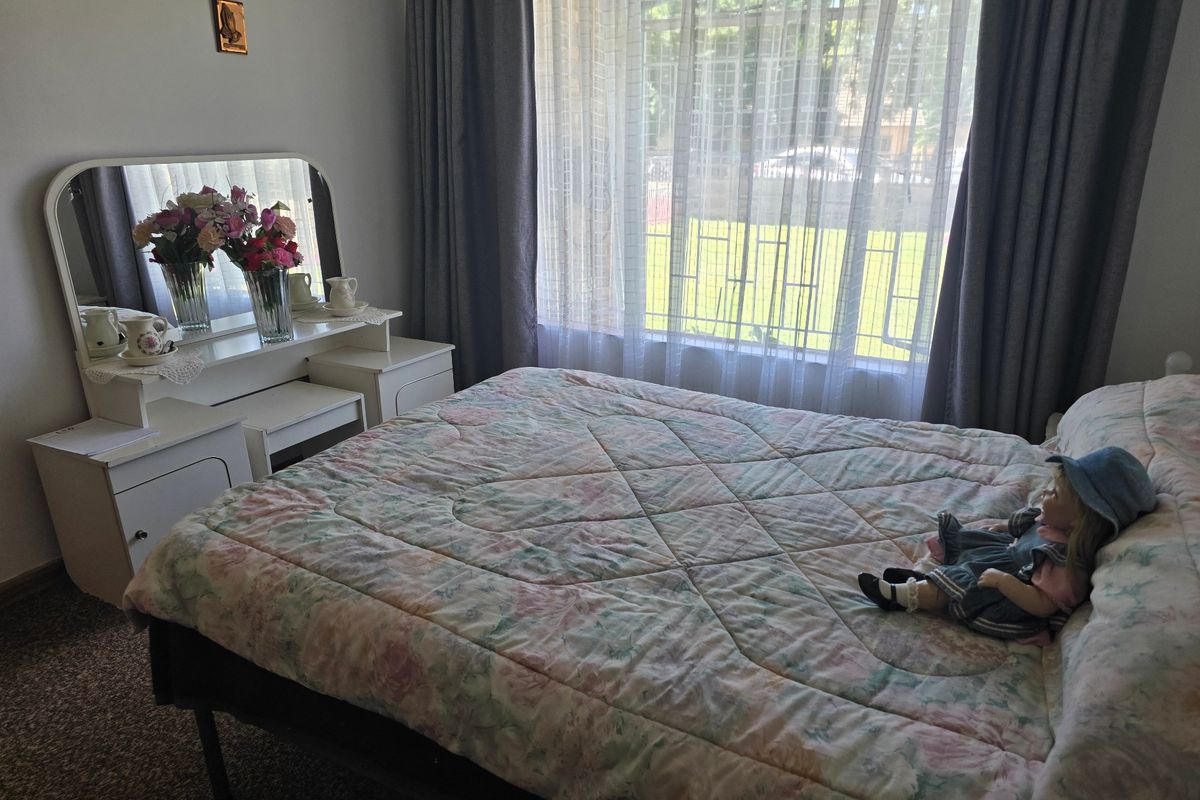 A bedroom featuring a large window with security bars and curtain rails, providing natural light and a view of the garden.