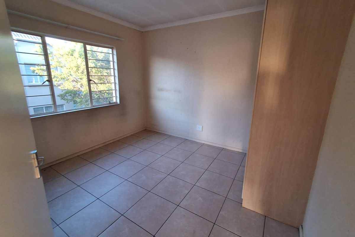 A vacant bedroom featuring tiled flooring, a built-in wardrobe, and a window fitted with security bars.