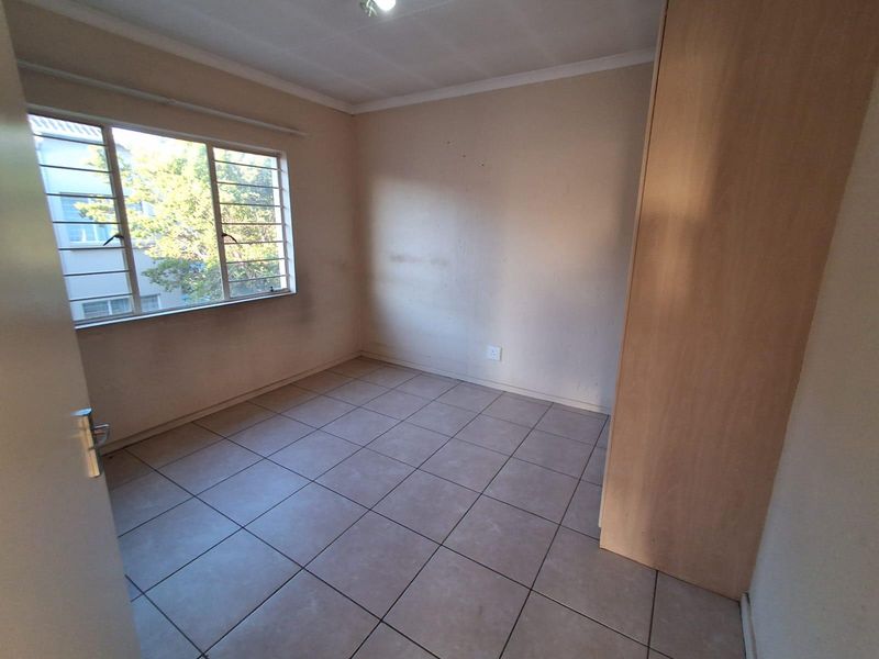 A vacant bedroom featuring tiled flooring, a built-in wardrobe, and a window fitted with security bars.