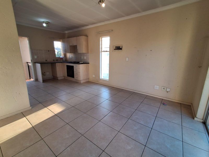 An open-plan living and kitchen area featuring tiled flooring, built-in cabinetry, and an integrated oven, offering a blank canvas for potential updates.
