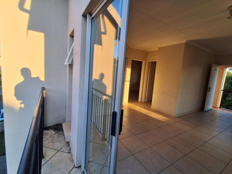 A spacious balcony area with tiled flooring and metal balustrade, providing access to the interior living space through a sliding glass door.