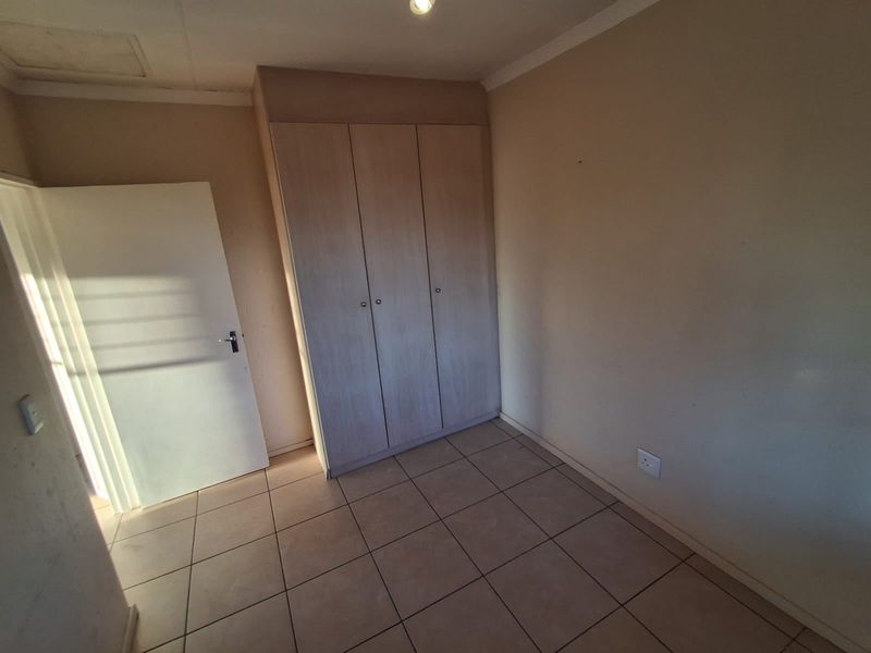 A vacant bedroom featuring neutral tiled flooring and built-in wooden cupboards, offering a clean and functional space ready for personalization.