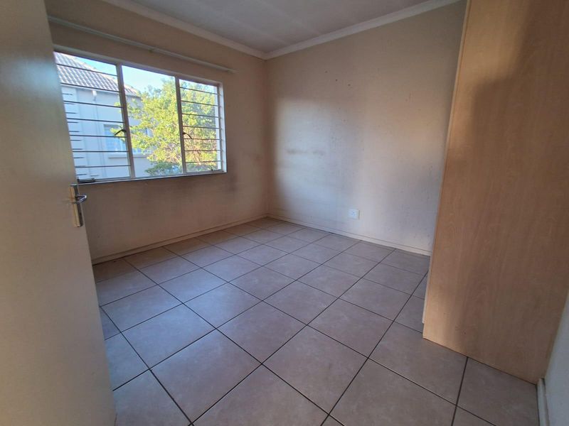 An empty bedroom featuring tiled flooring, a built-in cupboard, and a window with security bars. The walls require cosmetic attention.