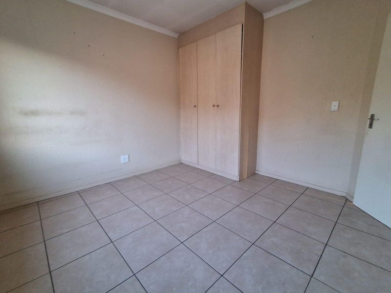 An empty bedroom featuring neutral tiled flooring and built-in wooden cupboards, providing a blank canvas for personalization.