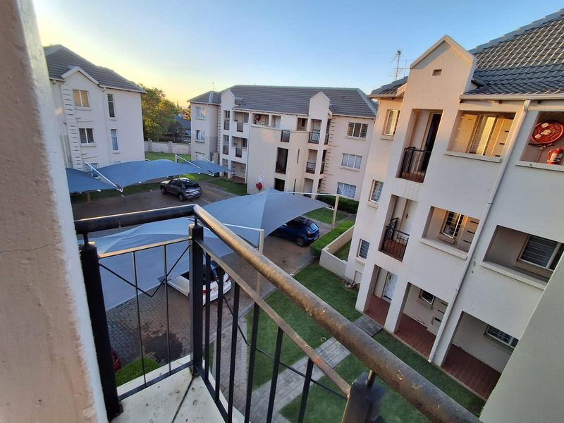 Elevated view from a balcony overlooking the apartment complex grounds, featuring paved parking areas with shade cloth carports and communal garden spaces.