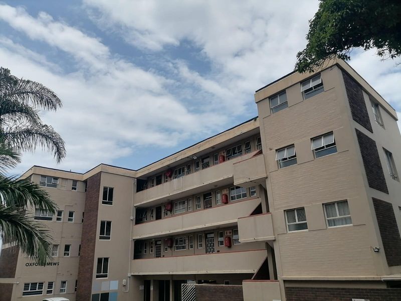 Exterior view of Oxford Mews apartment complex, featuring a multi-story brick facade with balcony walkways and standard casement windows.