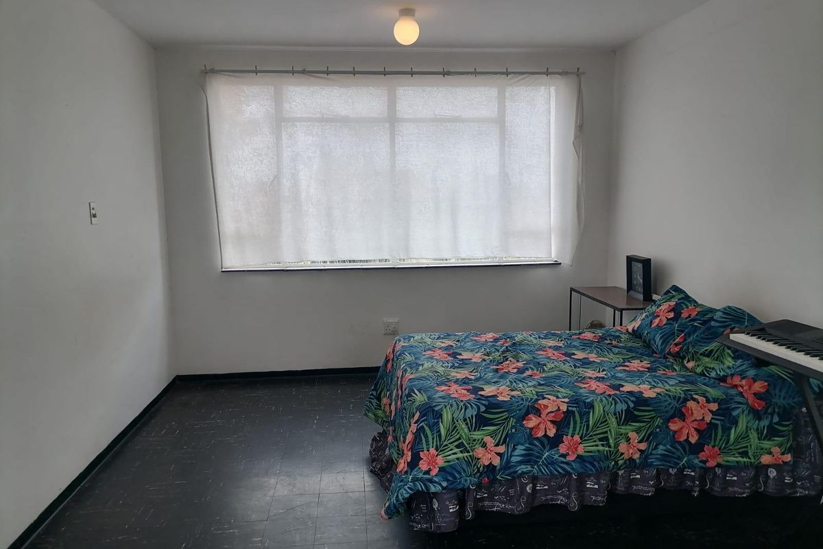 A simple bedroom featuring a large window, dark flooring, and basic lighting, offering a blank canvas for potential interior updates.