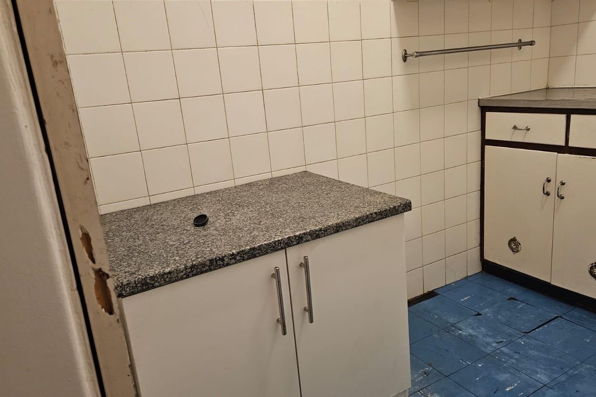A compact kitchen area featuring granite countertops, built-in cabinetry, and tiled wall splashbacks, currently requiring some maintenance and cosmetic updates.