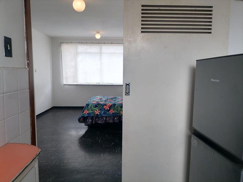 A view from a kitchen area into a bedroom featuring a sliding door with a ventilation grille and dark flooring.