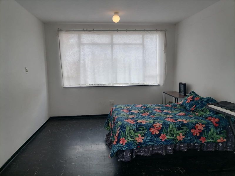 A simple bedroom featuring a large window, dark flooring, and basic lighting, offering a blank canvas for potential interior updates.