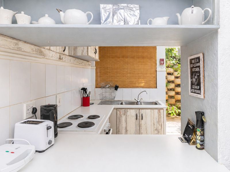 Compact scullery area featuring built-in cabinetry, a stainless steel sink, and an electric hob, providing functional prep space with direct access to the outdoors.