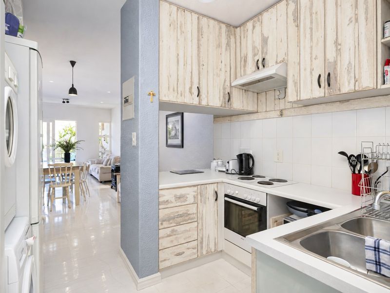 Compact kitchen featuring built-in cabinetry, electric hob, oven, and stainless steel sink, flowing into an open-plan living and dining area.