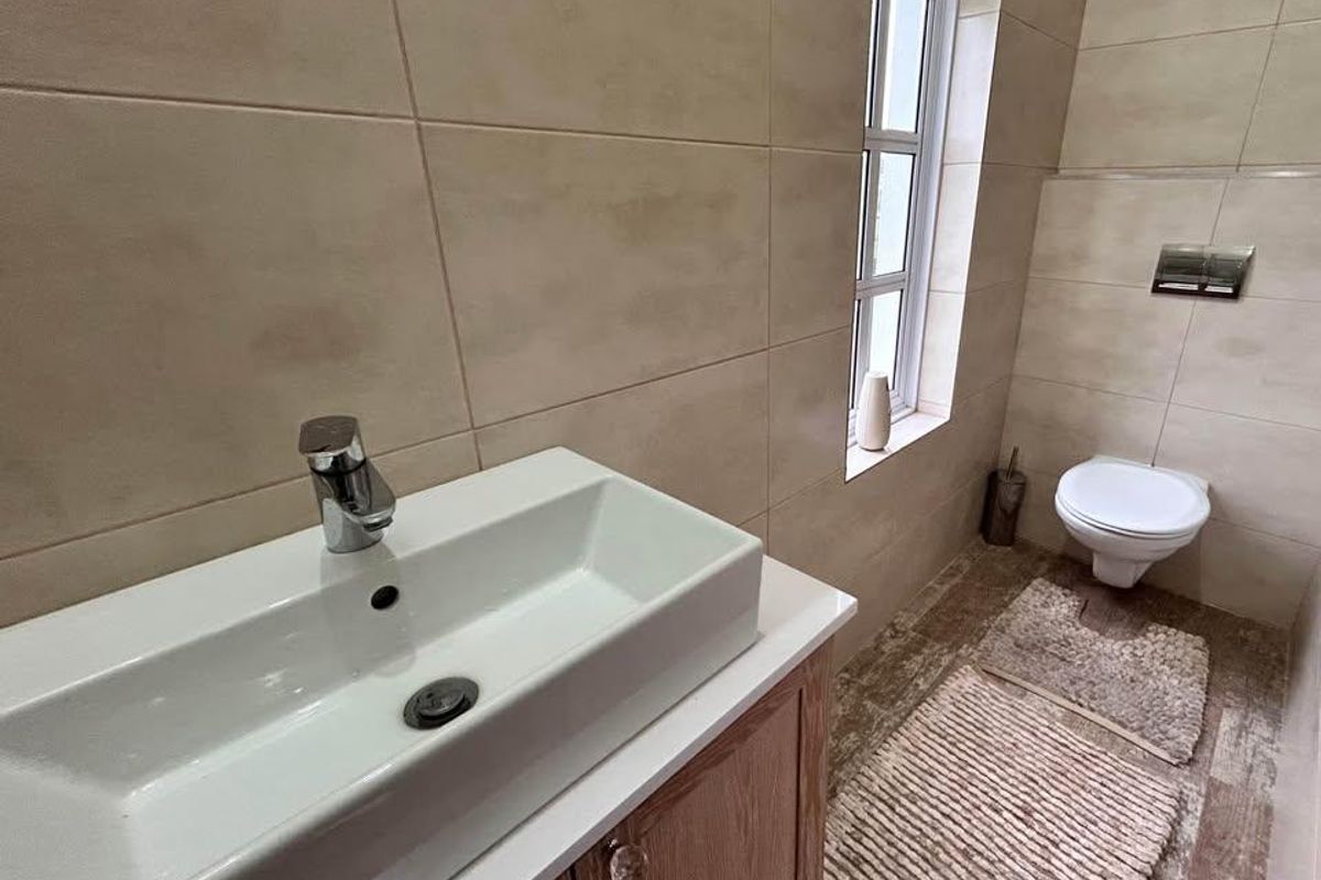 A modern bathroom featuring a wall-mounted toilet, a vanity cabinet with a vessel sink, and neutral-toned wall and floor tiling.