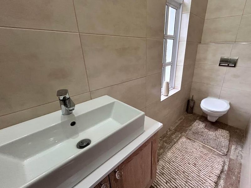 A modern bathroom featuring a wall-mounted toilet, a vanity cabinet with a vessel sink, and neutral-toned wall and floor tiling.