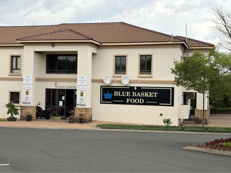Front exterior view of a commercial building featuring a tiled roof, stucco facade, and signage for a fitness centre and food store.