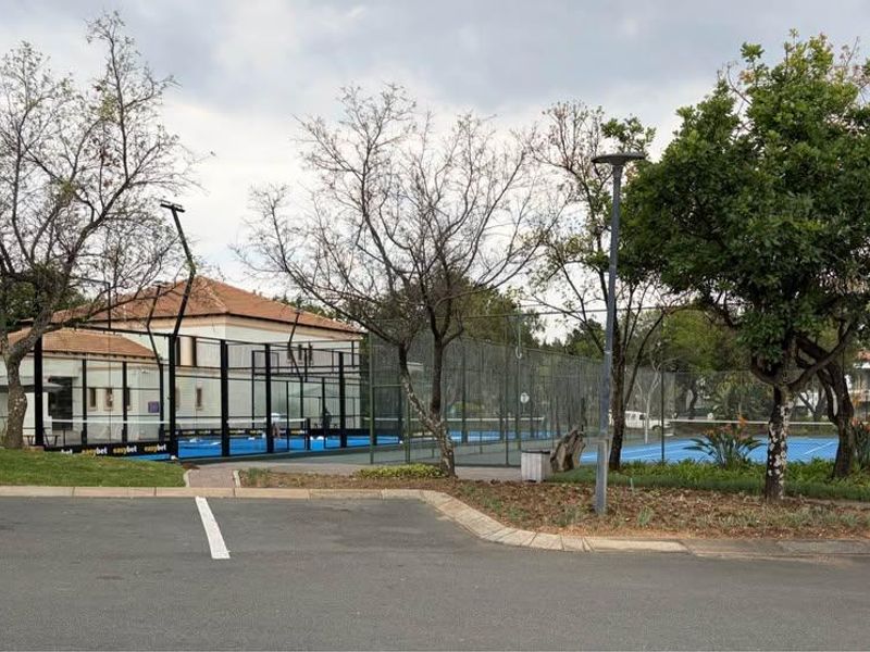 A well-maintained outdoor sports facility featuring fenced courts, adjacent paved parking, and established landscaping in a residential setting.