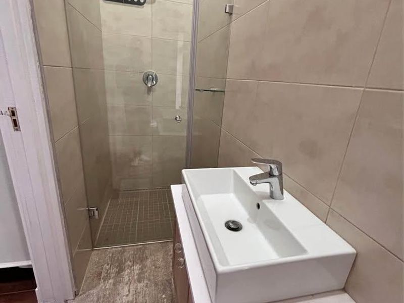 Modern bathroom featuring a vessel sink vanity, chrome fixtures, and a glass-enclosed shower with neutral wall and floor tiling.