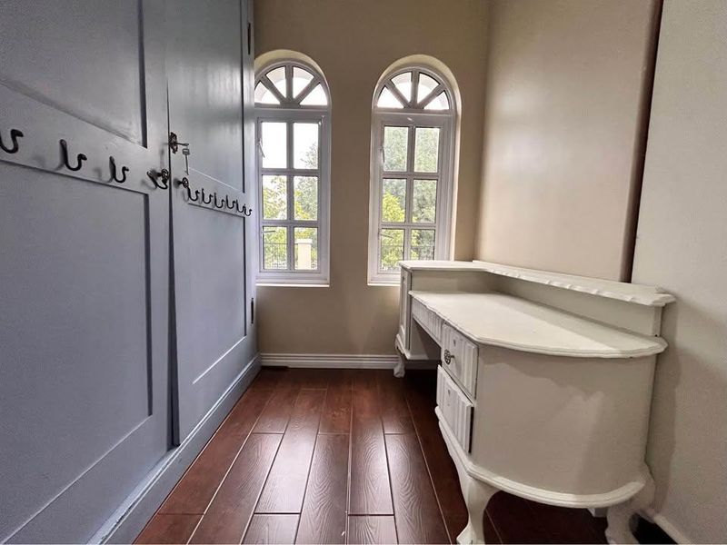 A bright hallway featuring elegant arched windows, dark laminate flooring, and built-in cabinetry, creating a functional and well-lit transition space.