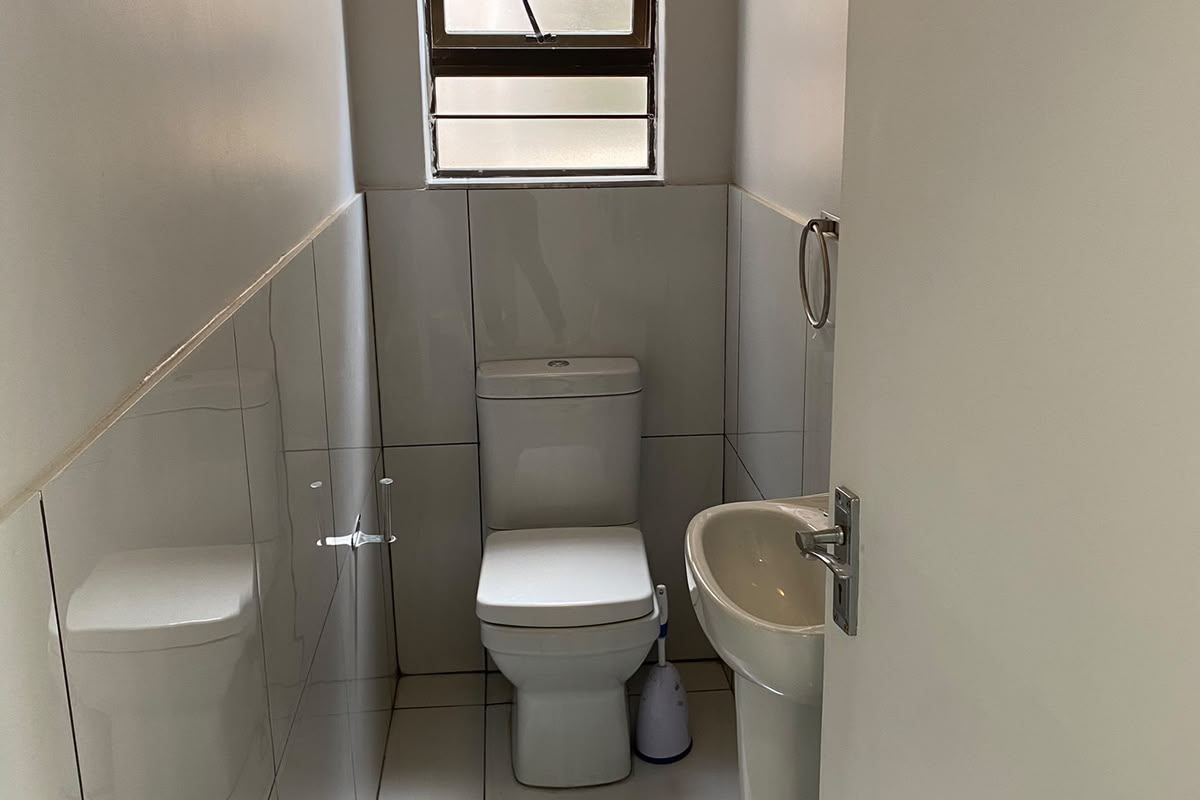 A compact guest bathroom featuring a white pedestal basin, toilet, and neutral wall and floor tiling with a louvered window for ventilation.