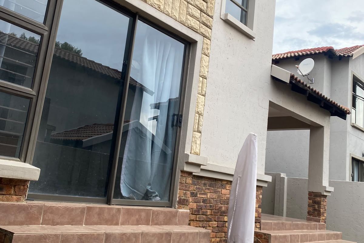 Rear exterior view of a townhouse featuring a tiled staircase leading to sliding glass doors, stone cladding accents, and a balcony.