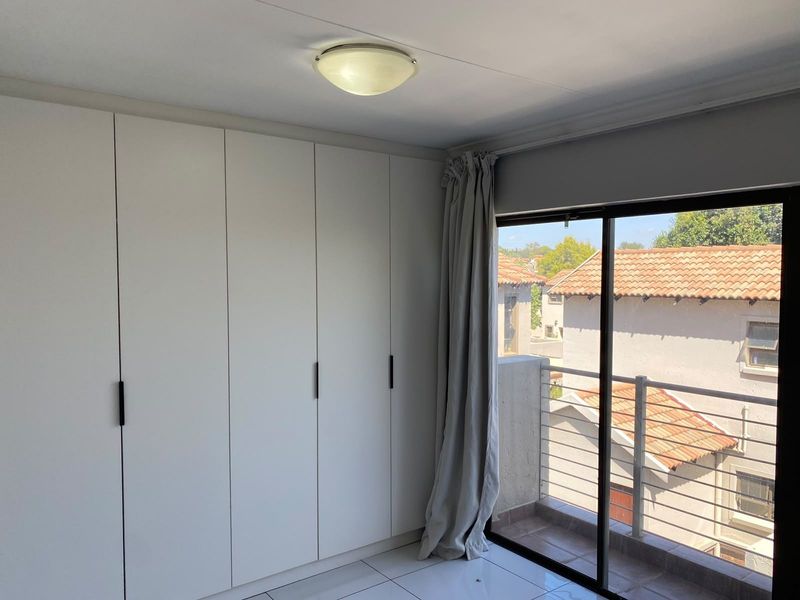 A bright, empty bedroom featuring built-in cupboards, tiled flooring, and a sliding glass door leading to a private balcony.