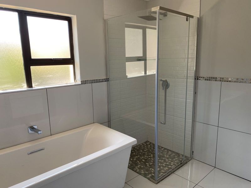 Modern bathroom featuring a sleek freestanding bathtub, a glass-enclosed shower with a rain shower head, and contemporary wall tiling with mosaic accents.