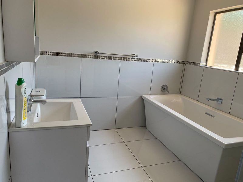 A clean and modern bathroom featuring a white vanity with basin, a bathtub with chrome fixtures, and neutral wall and floor tiling.