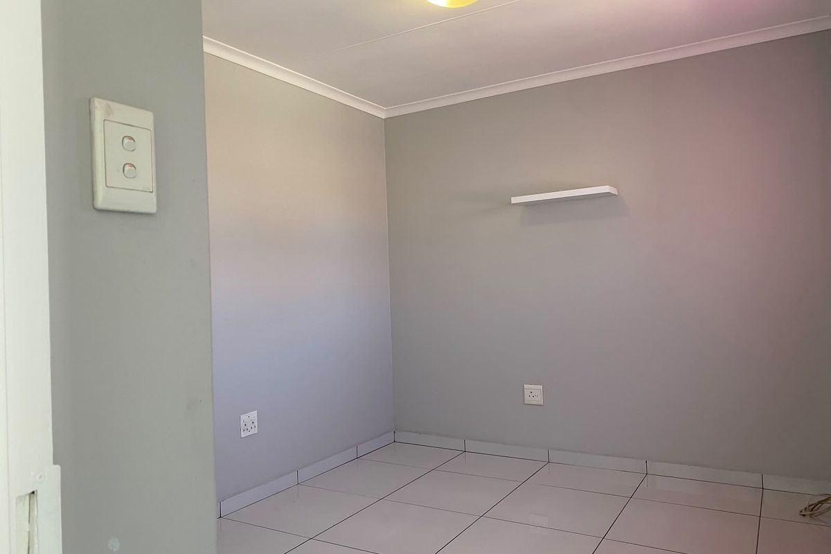An empty bedroom featuring neutral grey walls, white tiled flooring, and a wall-mounted shelf, providing a clean and versatile space.